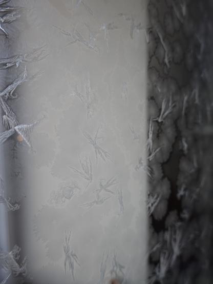 abstrakt wirkendes Foto, vertikal in unterschiedlichen Grautönen, unterbrochen von bizarren Eisblumenformen.