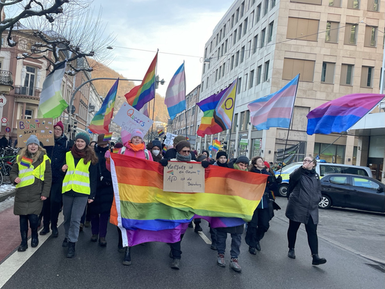 Bild von der Front des queerfeministischen Blocks mit großer Regenbogenflagge als Banner und vielen Fahnen
