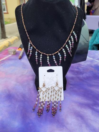 A chandelier earring and coordinating rainfall necklace. The earrings are made with 20g Antique Bronze finished copper and finished with dangle chains made with 2x3mm rondelle beads that shift from dark purple to clear AB. The necklace is made with 8/0 and 11/0 seed beads and with matching rondelle beads.