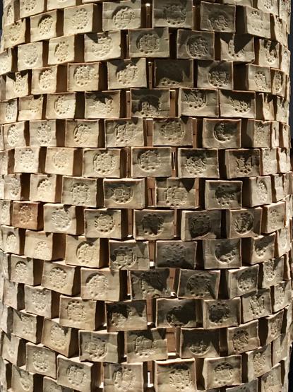 Photographie d’une partie d’une tour cylindrique réalisée à partir de l’empilement en quinconce de plusieurs dizaines de pains de savon parallélépipédiques de couleur brun-beige.