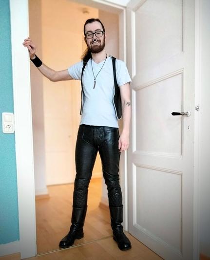 Me standing in a doorway wearing black leather boots, pants and vest with a white tshirt underneath.