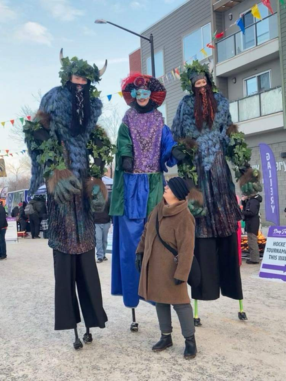 Senator Simons, in profile, stares up at three stilt walkers outside the Stollery Gallery.