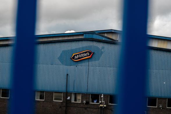 Photo of a warehouse seen through blue bars. There is a logo on the side reading "McVitie's". The blue paint of the warehouse has faded, but a lesser fade around the sign (in the same shape) suggests there was once a larger one in its place.