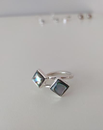 An open silver ring with two green square stones, each one in the other end.