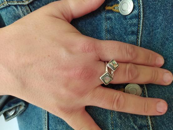 An open silver ring with two green square stones, each one in the other end. It's worn by a woman