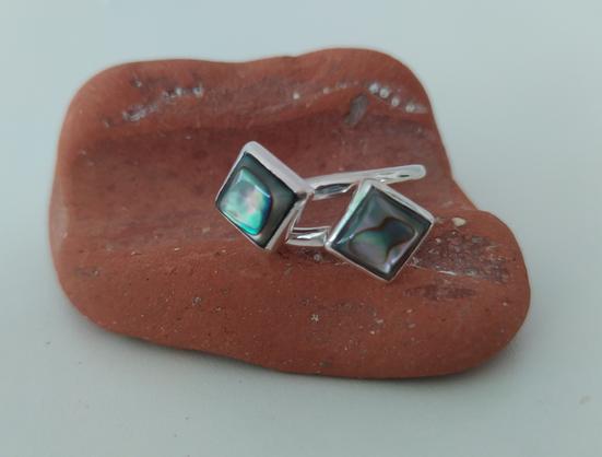 An open silver ring with two green square stones, each one in the other end. It is placed on broken brick