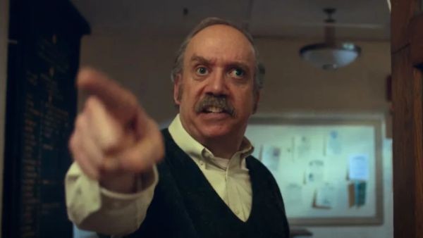A still from the film The Holdovers. A cross-eyed middle-aged white man stands in front of a noticeboard wearing an angry impression and pointing his finger.