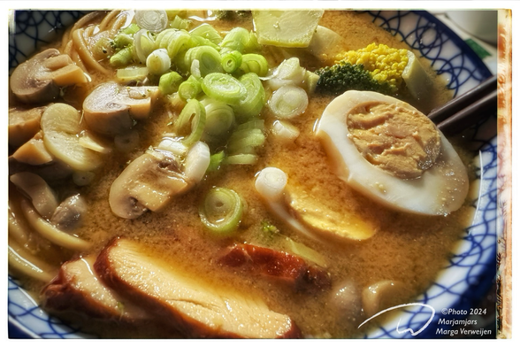 Foodphoto of japanese dish with miso udon noodle soup with smoked chicken, soy egg, broccoli, mushrooms, garlic slices and spring onions.