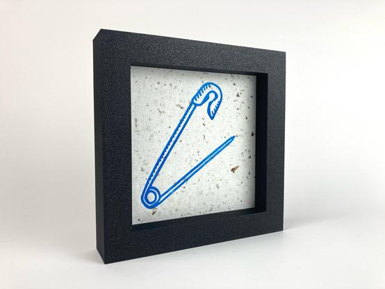 A framed relief print of a safety pin.
