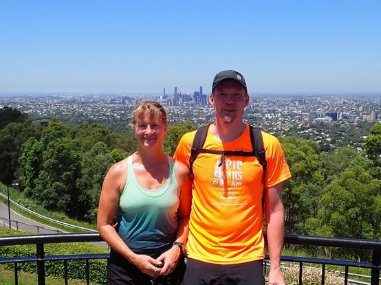 Portrait of guy in an orange top and lady in green vest with the city of Brisbane behind under clear blue skies
