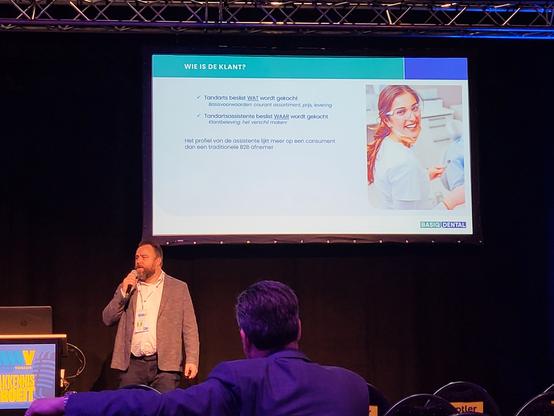 Willem Schilders presenteert namens Basiq Dental over de uitdaging tussen Marketing (Vraag) en Supply Chain Management (Aanbod) tijdens de #WebWinkelVakdagen 2024. Op de slide is een tandartsassistente te zien en de resultaten van intern markt onderzoek naar de klantreis. Basiq Dental er achter kwam dat de tandarts bepaalt WAT gekocht wordt, maar de assistente WAAR gekocht wordt. Daarom is het idee van een klassieke business-to-business webshop losgelaten en een webshop ontwerp toegepast die meer lijkt op een consumenten webshop zoals #CoolBlue