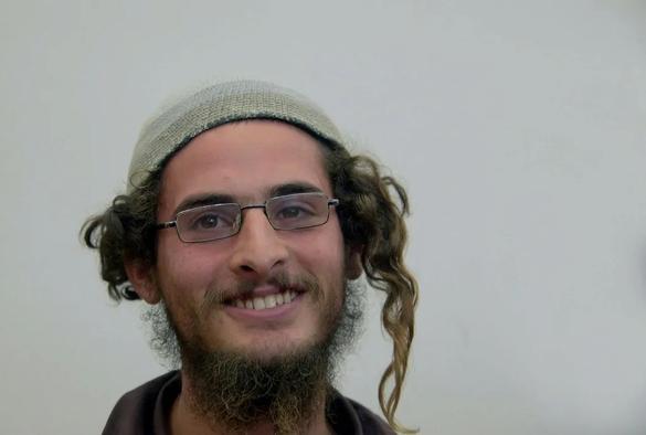 A smiling man with glasses, curly hair, and a beard wearing a knitted cap on a plain background. Meir Ettinger, Meir Kahane’s grandson and leading ideologue of the hilltop youth