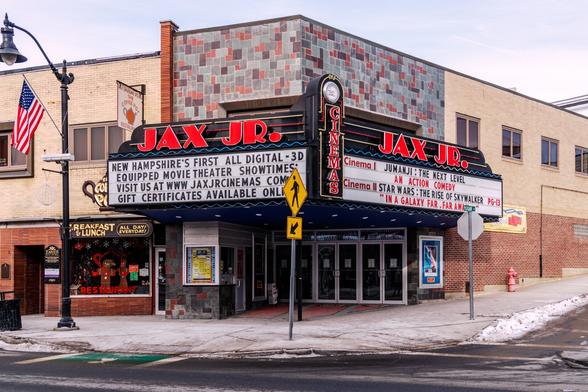 A color photograph of a downtown movie theater on a corner. The marquee lists “Jumanji: The Next Level” as “An Action Comedy” and “Star Wars: The Rise of Skywalker” as “In a Galaxy Far, Far Away”.  The other sign face touts them  as being the first all digital projector theater in New Hampshire and says gift certificates are available.

Next door to the left, a breakfast/lunch restaurant  called “The Coffee Pot” has a window decorated for Christmas and a sign shaped like a water/tea kettle over the storefront. An American flag hangs from a light post on the street, and some dirty snow lined the curb.