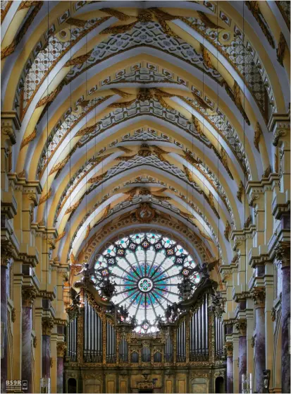Das Foto im Hochformat zeigt einen Teil vom Deckengewölbe des Mittelschiffs der Klosterkirche. Im Hintergrund ist die große, im gotischen Stil gehaltene Fensterrose mit der darunter befindlichen Hauptorgel bestehend aus Orgelpfeifen und Spieltisch zu sehen.

The photo in portrait format shows part of the vaulted ceiling of the nave of the monastery church. In the background you can see the large, Gothic-style rose window with the main organ below, consisting of organ pipes and console.