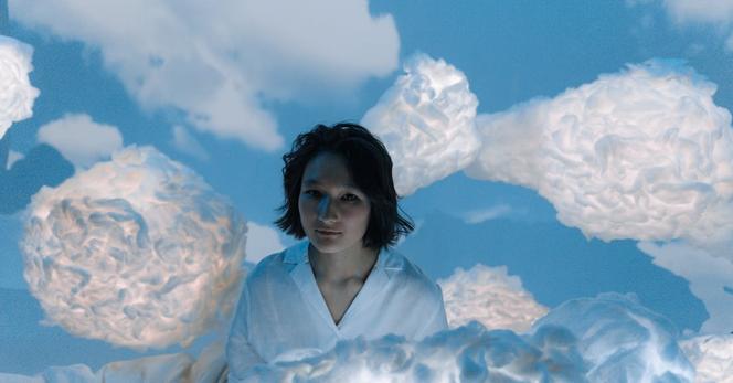 Image of the upper portion of a woman wearing a white blouse apparently floating among clouds.