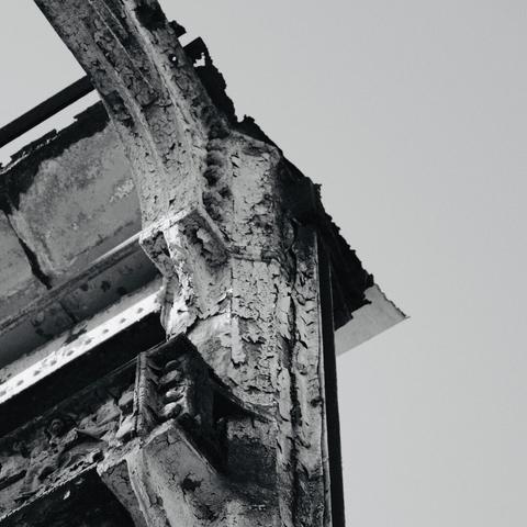 Alt text: A black and white photo of the corroded corner of a metal structure, showcasing the textures of decay and the passage of time.