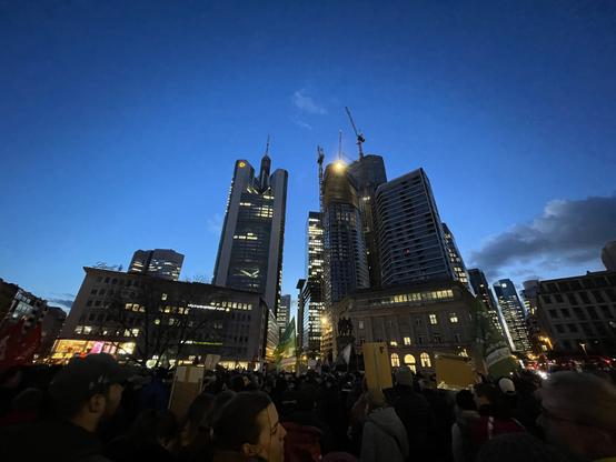 Weitwinkelsufnahme der Frankfurter Skyline in Abenddämmerung mit einer Menschenmenge am unteren Rand