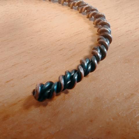The photo shows one end of the bangle.  The end has been rounded down with a file, revealing the copper colour.  The radially outermost surface of the twist has had the patina wiped away, more than the innermost surfaces.
