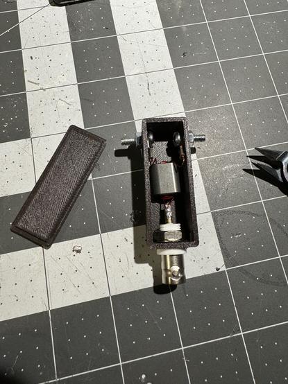 A small 3d printed box with a BNC connector, binocular toroid with copper wire wound in it and two screw posts on a project mat background.