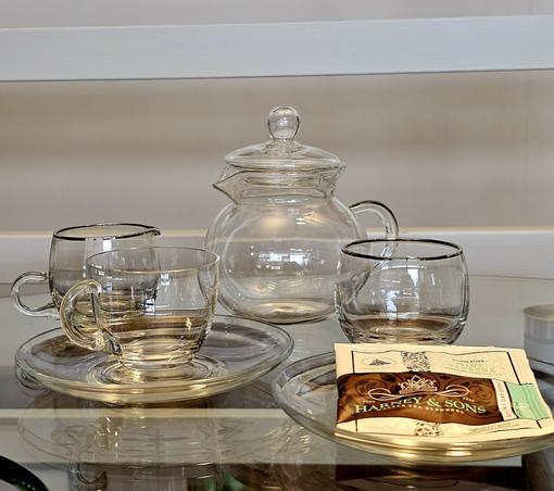 A tea tableau with clear glass teaware on a clear glass table. The tea is Mint Verbena herbal from Harney and Sons.