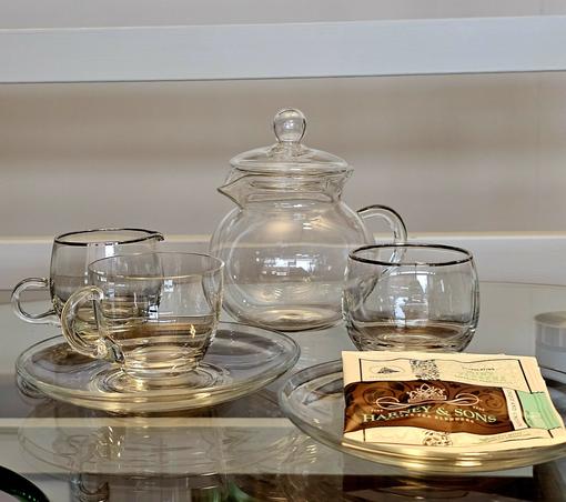 A tea tableau with clear glass teaware on a clear glass table. The tea is Mint Verbena herbal from Harney and Sons.
