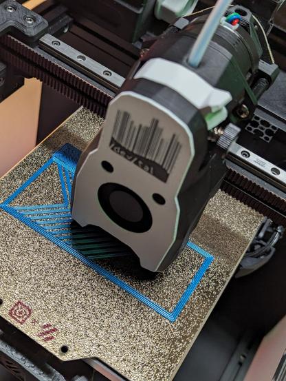 Das innere eines 3D Druckers. Zu sehen ist der Druck eines blauen Fischgrätenmusters. Es dient als Testdruck für die Kalibrierung des Druckers. Der Printhead hat das Logo des devtal e.V. integriert.