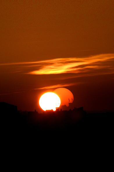 A photo of a sunset taken straight into the Sun, setting behind the city castle and projecting the second, phantom Sun and the castle tower silhouette side by side with the real one onto the double pane window the photo was taken through.