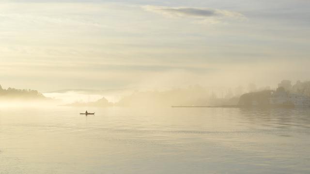 A photo of a kayaker in the fog. There are some small islands behind them. The sky is cloudy.