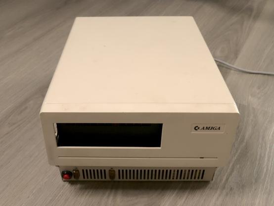 Top-front view of the Sidecar. It looks a bit like an odd PC case of the late 1980s. Only the "AMIGA" badge on the front reveals that it is somehow Amiga related.

There is an opening for a 5¼" disk drive, but it's empty. There is also a red button at the bottom left edge of the front.