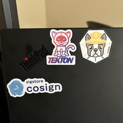 Lenovo Thinkpad with Tekton robocat, Buildah Boston terrier, and sigstore cosign stickers.