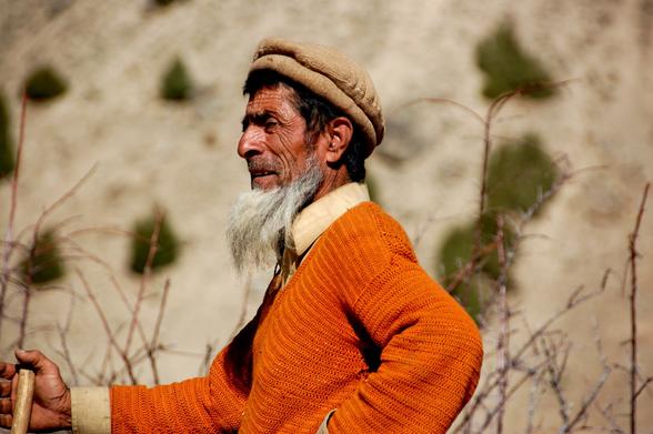 Photo of an elderly Burusho man standing in profile. His face has deep wrinkles and he has a grey beard.