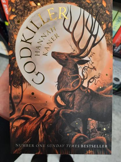 Book - Godkiller - by Hannah Kaner. Cover features a beautiful stag and a moon in the background. The title and author's name is in gold, set within the moon.