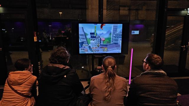Vier Menschen von hinten beim Spielen von Super Mario Smash Bros. auf einer N64 in der Lobby des Kongresses.