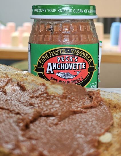 Peck's Anchovette bottle standing behind a piece of toast that is smeared with fishpaste
