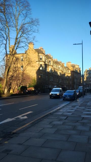 A line of Victorian stone tenements, side wall and upper storeys in golden, winter light, lower parts in shadow