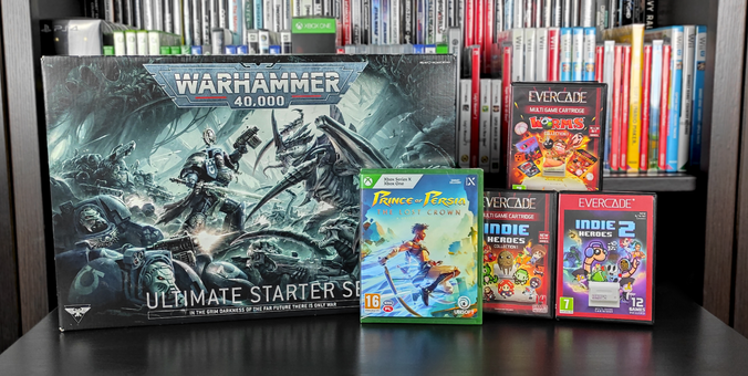 Zdjęcie z comiesięcznymi zdobyczami. Po lewej stronie - pudło zawierające starter do 10-edycji gry figurkowej "Warhammer 40.000" w edycji Ultimate. Pośrodku - pudełko z grą "Prince of Persia: The Lost Crown" na konsolę XBOX Series X oraz XBOX One. Po prawej stronie, na froncie, od lewej - pudełko z kartridżem z grami "Indie Heroes Collection I" oraz pudełko z kartridżem z grami "Indie Heroes 2" na konsolę EVERCADE. Tylny rząd - pudełko z kartridżem z grami "Worms Collection I" na konsolę EVERCADE.