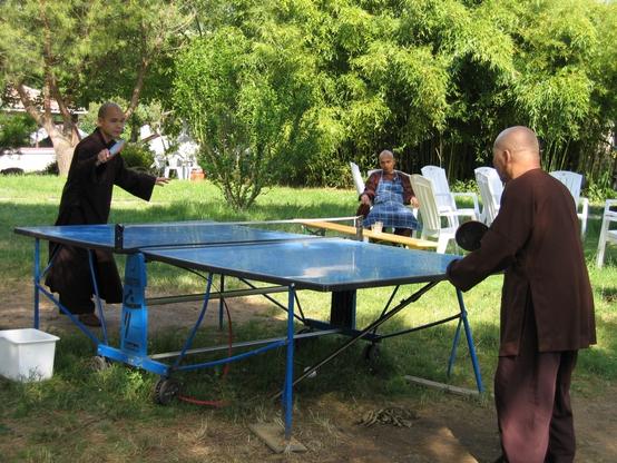 Two monks play ping pong ball while a third monk looks on, in Plum Village 2004.