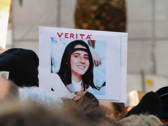 another sign ;    it's the text  "VERITÀ"  ('Truth')   and  below it  a famous picture of Emanuela ;   she's smiling,  she's got  long straight dark hair  and wearing a bandana on the forehead