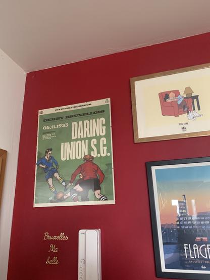 A red wall in our living room, with diverse posters about Brussels, one a historic motif from an Union - Daring derby