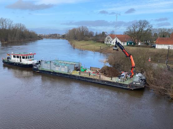 Aufräumarbeiten an der Weser. Mit einem großen Baggerarm auf einem Deckprahm wird Treibgut, das sich am Ufer verfangen hat vom Wasser aus aufgenommen.