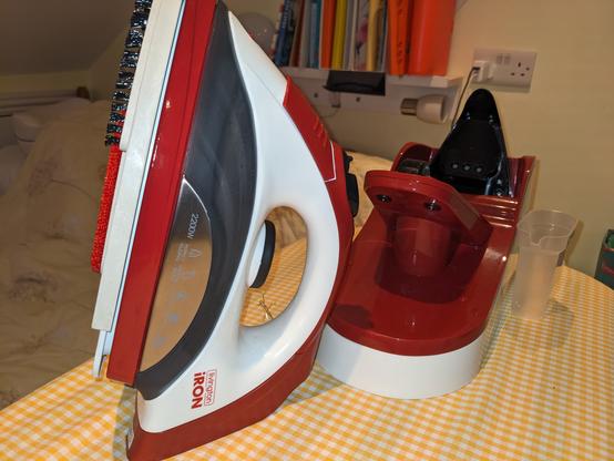 A red and white clothes iron; you can see the basic iron you hold, the brushes on the soleplate, and the huge docking/charging station which clamps to the ironing board.