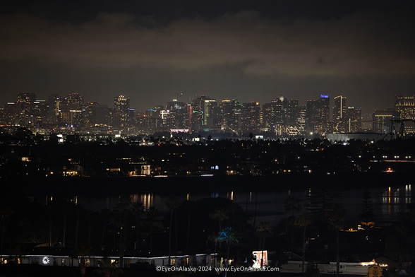 A night shot of downtown San Diego in the distance with lights reflecting in Mission Bay in the foreground.