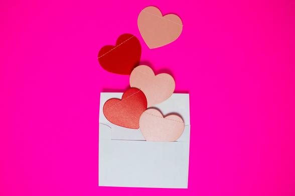 Graphic of a white envelope - opened - with pink and red hearts coming out of it. The background is a bright pink.