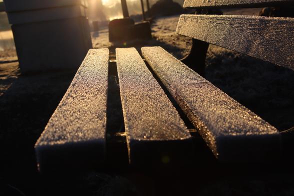 Holzplankenbank, deren Holzplanken rauhreif aufzeigen  und die morgendliche Sonne lässt das Ganze schön funkeln.
Matze-work