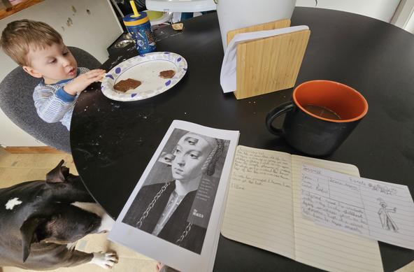 A wide angle image of a dining room table, upon which sits a printed-out copy of The Magus and a small notebook next to a mug of coffee.

Off to the left, a toddler is eating breakfast which he has helpfully smeared across the table.

A dog sits next to the toddler, waiting for the inevitable scraps to fall.