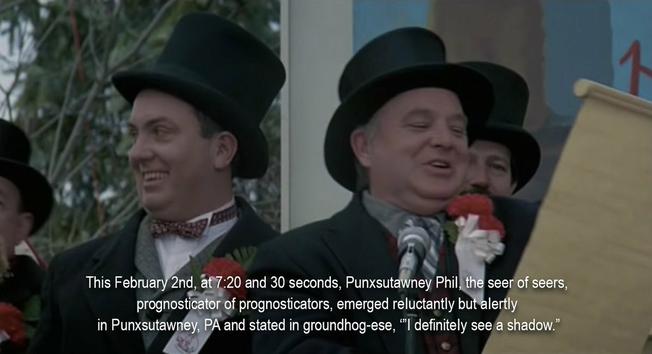 Two men in top hats, wearing carnations in their lapels, reading from a scroll. The subtitle reads, “This February 2nd, at 7:20 and 30 seconds, Punxsutawney Phil, the seer of seers, prognosticator of prognosticators, emerged reluctantly but alertly in Punxsutawney, PA and stated in groundhog-ese, "I definitely see a shadow.””