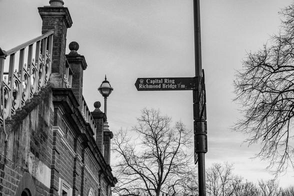 A 'fingerpost' signpost points at a brick bridge with a metalwork banister. The fingerpost reads 
'Capital Ring 
Richmond Bridge ½ m'