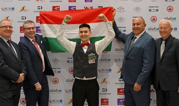 Révész Bulcsú hebt jubelnd beide Fäuste. Hinter ihn wird die ungarische Flagge gehalten, Dazu stehen vier Funktionäre, darunter Jason Ferguson, um ihn herum.