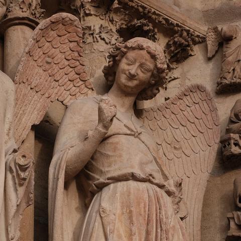 A close-up of a smiling stone angel, exuding charm and serenity from the facade of a gothic cathedral.