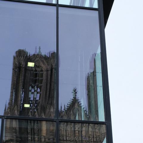 The reflection of a gothic cathedral's spires in a modern glass facade, a juxtaposition of history and modernity.